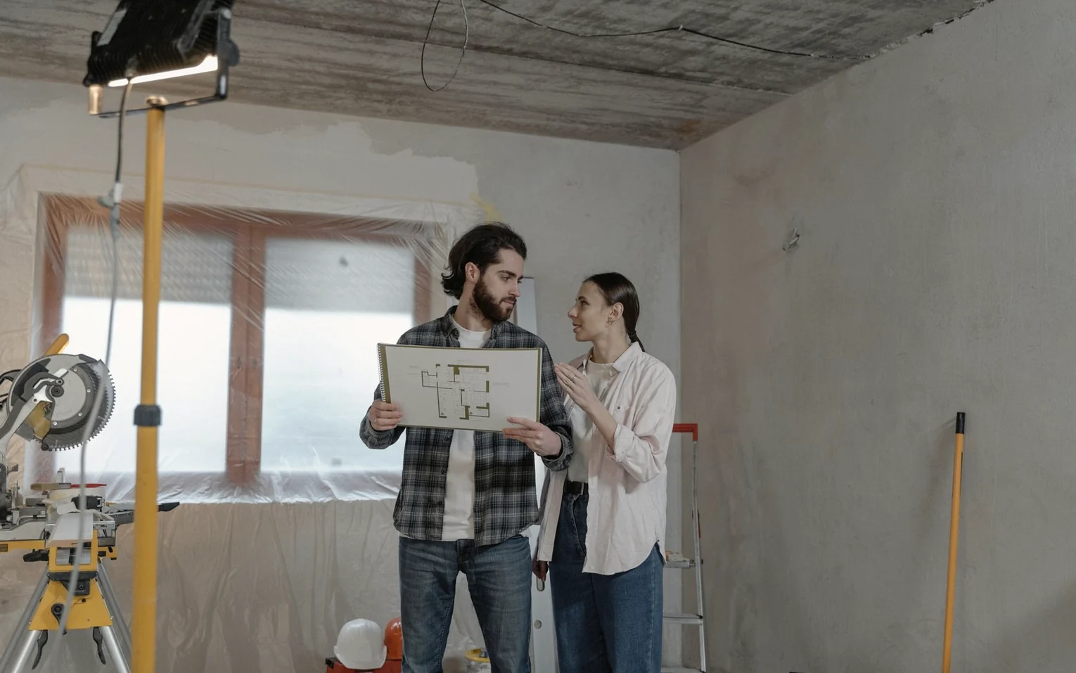 Zwei Personen besprechen einen Grundriss in einer leeren Fläche
